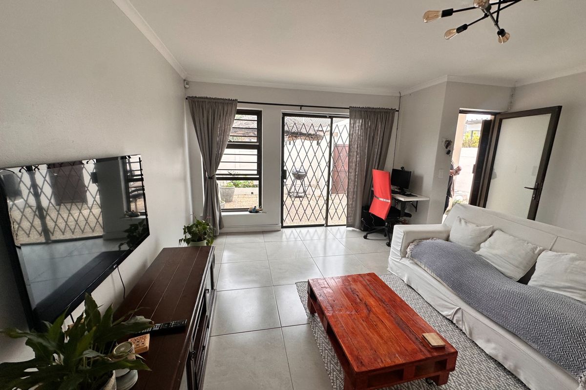 A bright and well-maintained living room featuring tiled flooring, modern lighting, and a sliding glass door providing access to the outdoor area.
