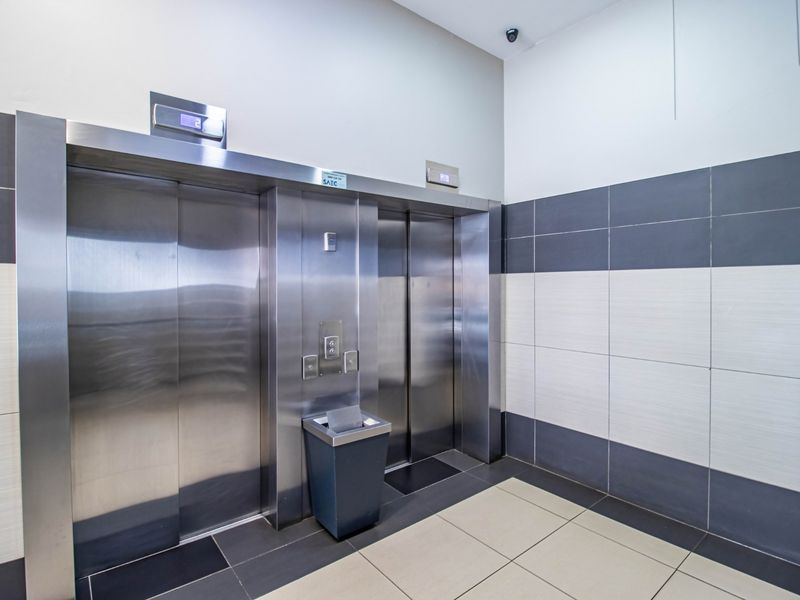 A clean commercial elevator lobby featuring stainless steel lift doors, modern two-tone ceramic wall tiling, and durable floor tiles.