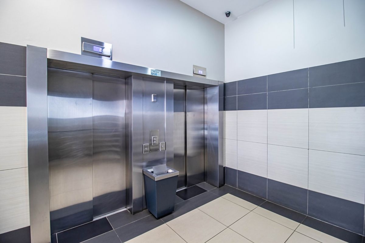 A clean commercial elevator lobby featuring stainless steel lift doors, modern two-tone ceramic wall tiling, and durable floor tiles.