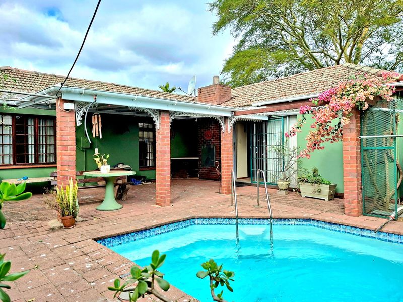 Outdoor pool area featuring a covered patio with brick pillars, paved surround, and direct access to the main residence.