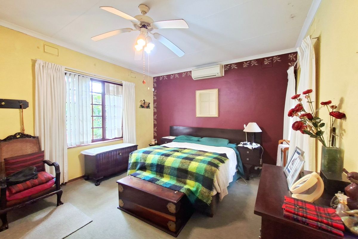 A spacious bedroom featuring a ceiling fan, split-system air conditioning, and large windows with blinds, offering a comfortable and functional living space.