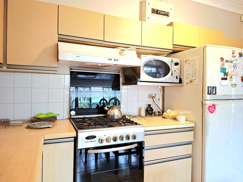 A functional kitchen featuring a gas stove, extractor fan, built-in microwave, and laminate cabinetry with a tiled splashback.
