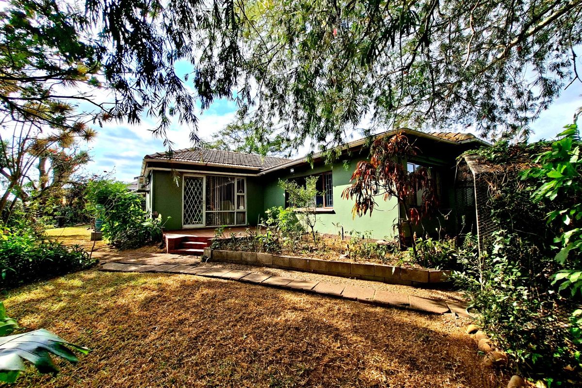 Rear view of the house featuring a concrete patio, sliding glass doors with security gates, and a garden area with mature trees.