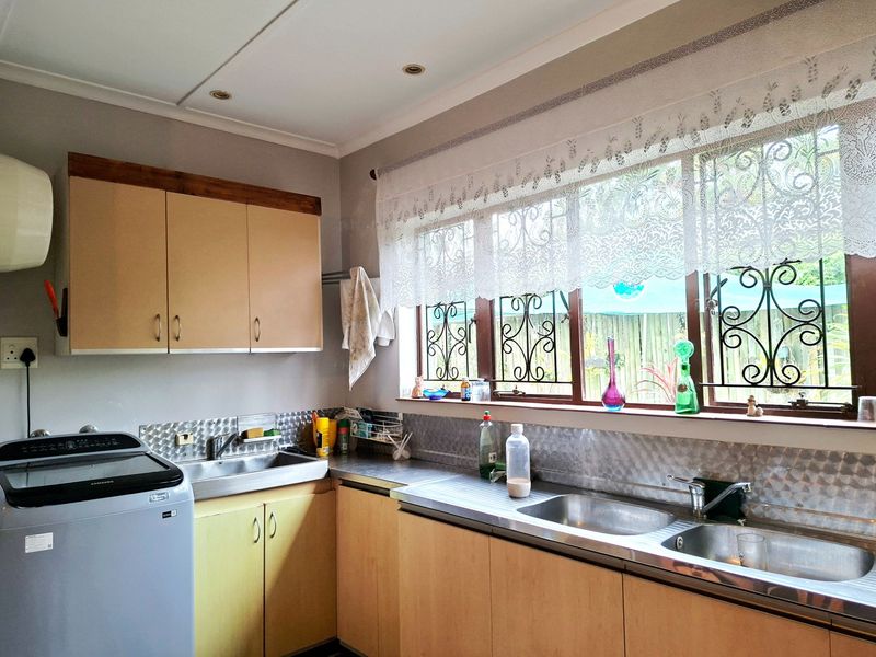 Functional scullery area featuring double stainless steel sinks, metal splashbacks, and ample laminate cabinetry with natural light from large windows.