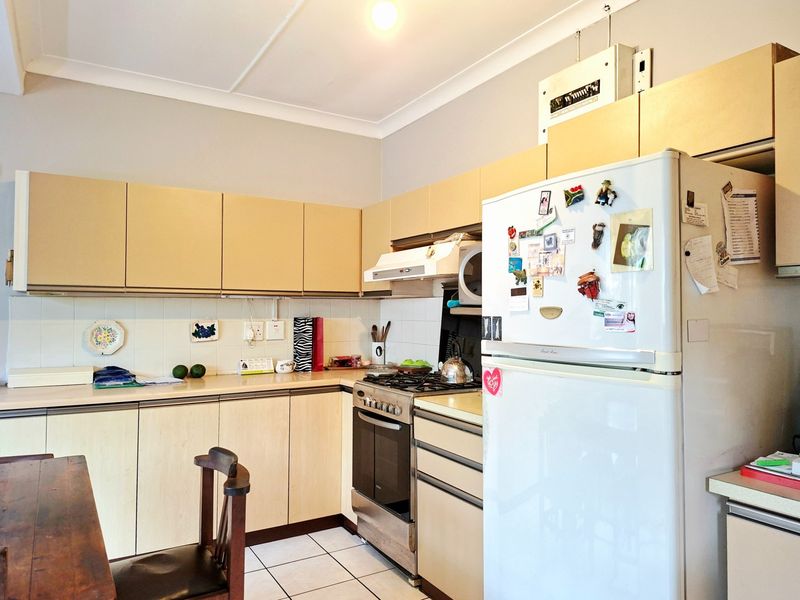 Functional kitchen featuring light-toned laminate cabinetry, tiled backsplash, gas stove with extractor fan, and tiled flooring.