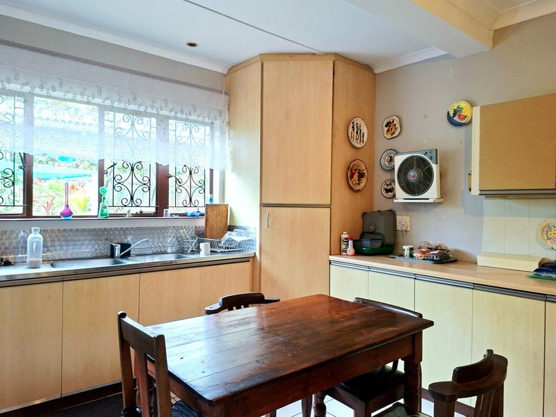 A functional kitchen featuring light wood-tone cabinetry, laminate countertops, a stainless steel double sink, and a tiled splashback with security-barred windows.
