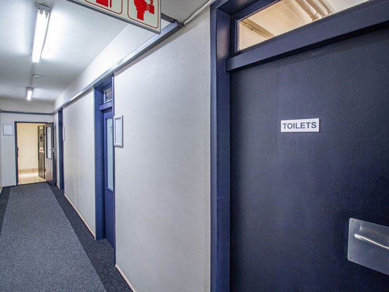 A commercial hallway featuring carpeted flooring, fluorescent lighting, and access doors to office or restroom facilities.