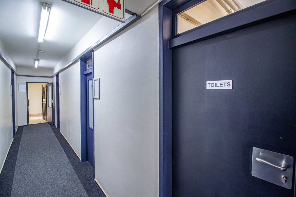 A commercial hallway featuring carpeted flooring, fluorescent lighting, and access doors to office or restroom facilities.