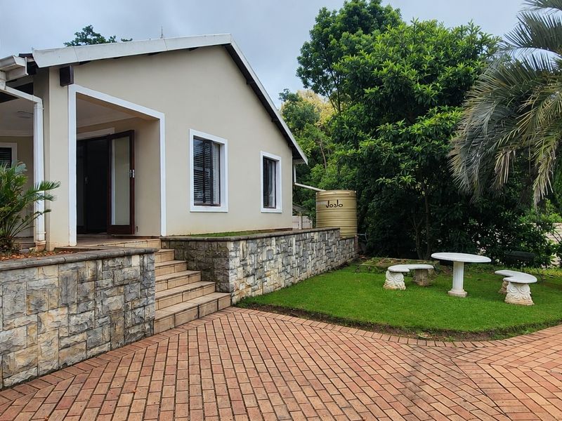 Rear exterior view of the cottage featuring a stone-clad retaining wall, brick paved patio area, swimming pool, and a water storage tank.