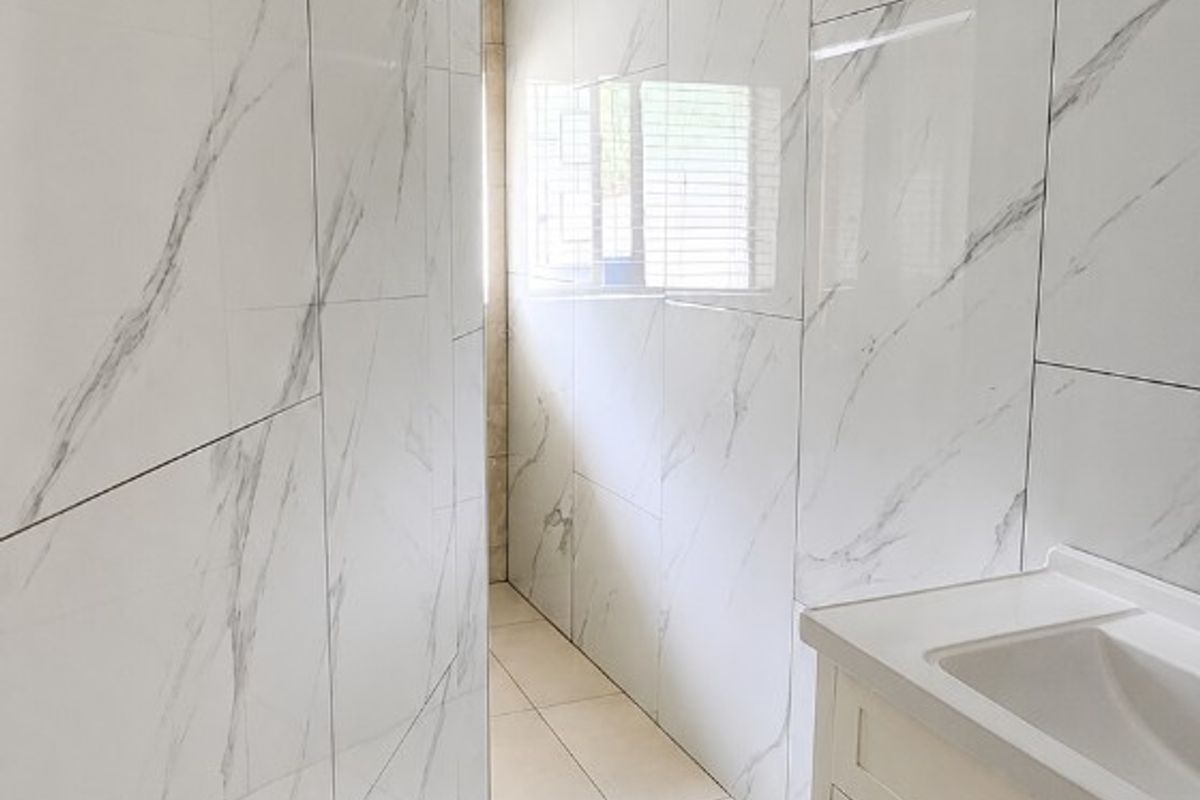 A compact bathroom featuring modern marble-look wall tiles, a white vanity cabinet with an integrated sink, and neutral floor tiling.