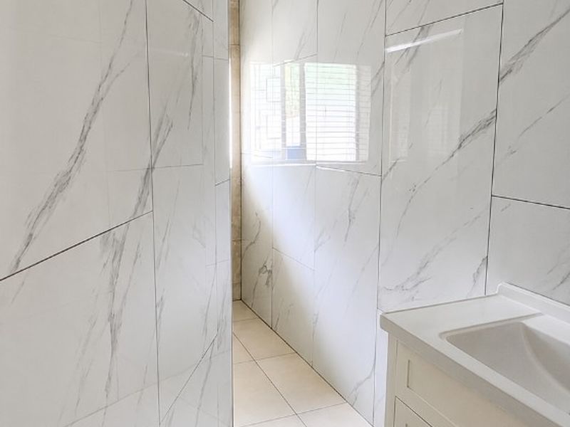 A compact bathroom featuring modern marble-look wall tiles, a white vanity cabinet with an integrated sink, and neutral floor tiling.