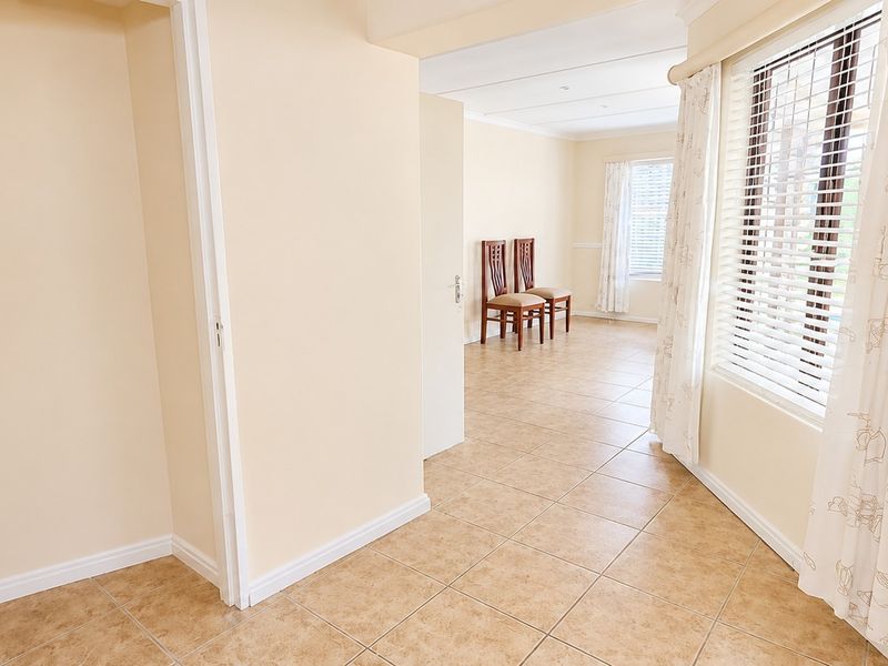 An open-plan living area featuring neutral wall tones, tiled flooring, and large windows with fitted venetian blinds, offering a bright and versatile space.