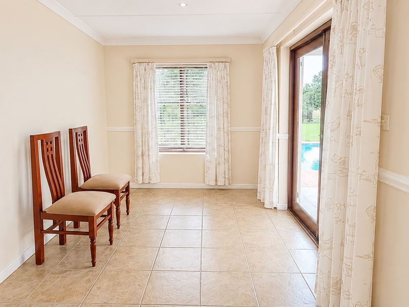 A bright, neutrally finished living area featuring tiled flooring, chair rail molding, and a sliding glass door providing access to the outdoor pool area.
