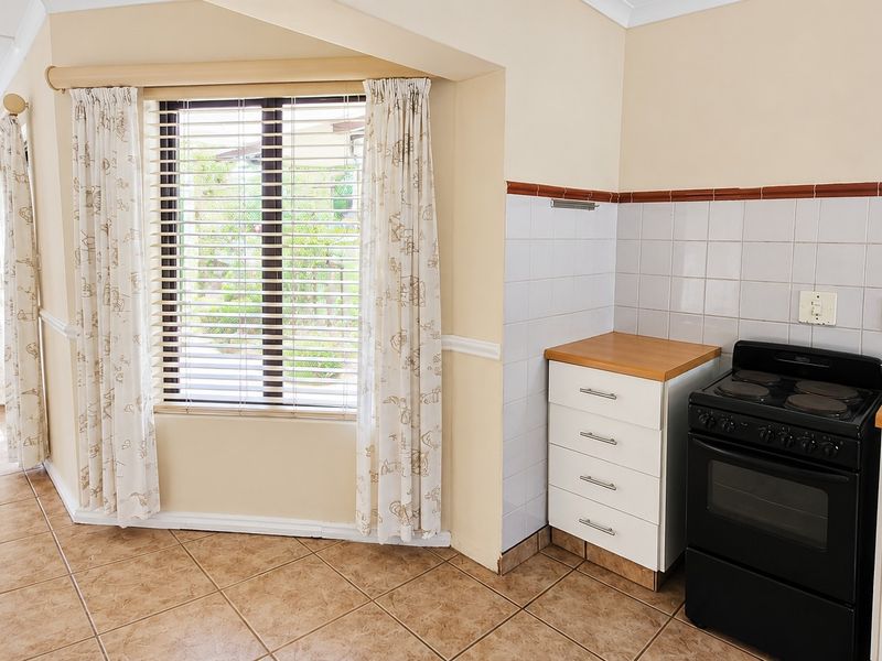 A functional kitchen area featuring tiled flooring, built-in cabinetry with laminate countertops, a tiled splashback, and a freestanding stove.