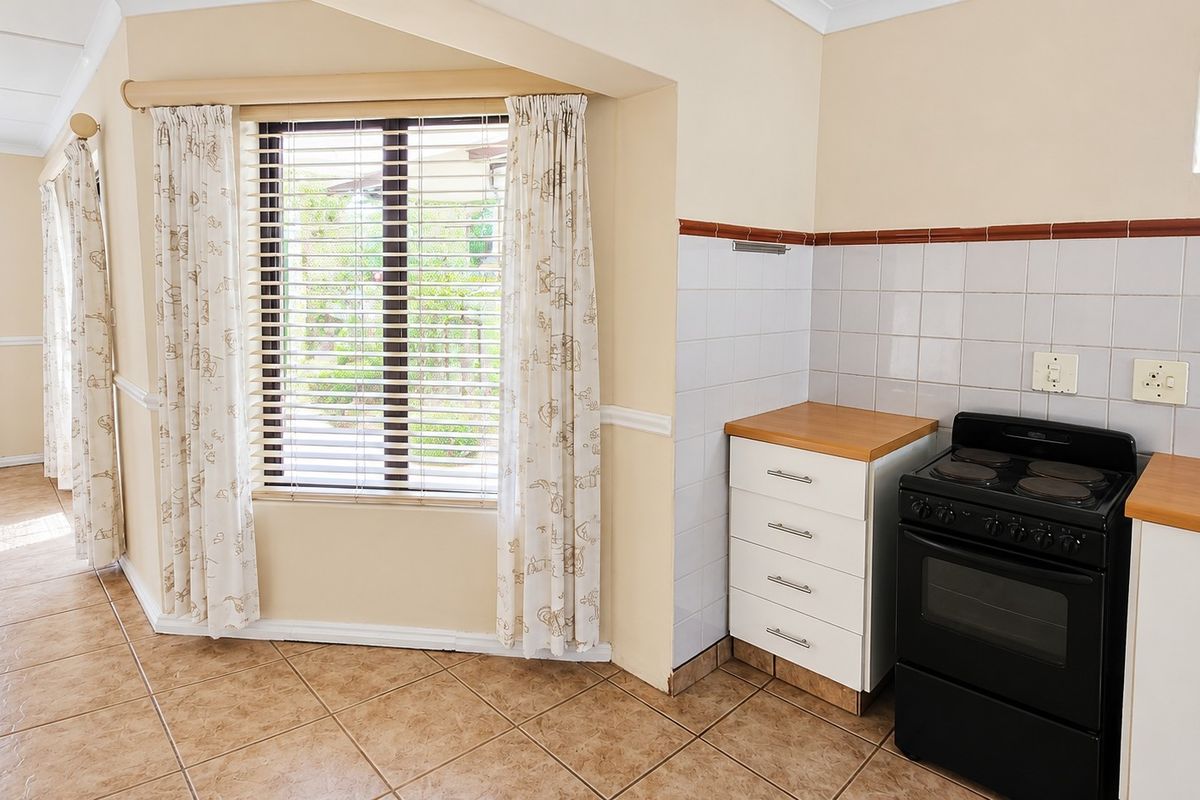 A functional kitchen area featuring tiled flooring, built-in cabinetry with laminate countertops, a tiled splashback, and a freestanding stove.