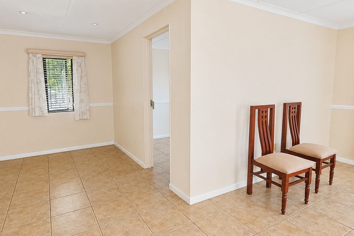 A bright, neutral living area featuring tiled flooring, recessed lighting, and decorative chair rail molding, offering a clean and versatile space.