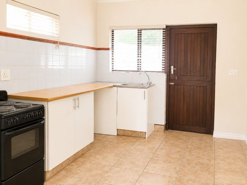 A functional kitchen featuring white cabinetry, laminate countertops, tiled splashbacks, and ceramic floor tiles, with direct access to an exterior door.