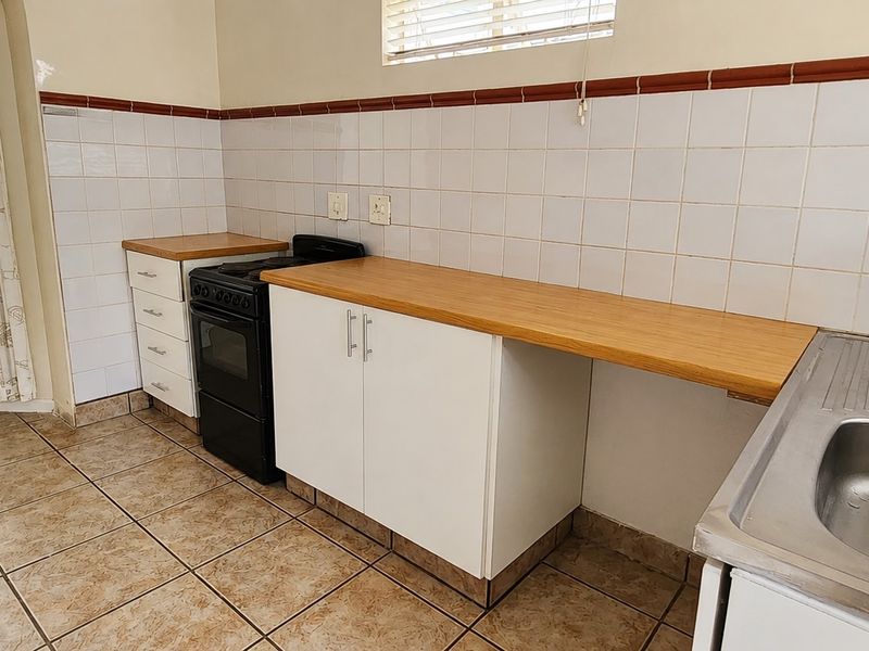 A functional kitchen featuring tiled flooring, white cabinetry with wooden countertops, a freestanding stove, and a stainless steel sink with tiled splashbacks.