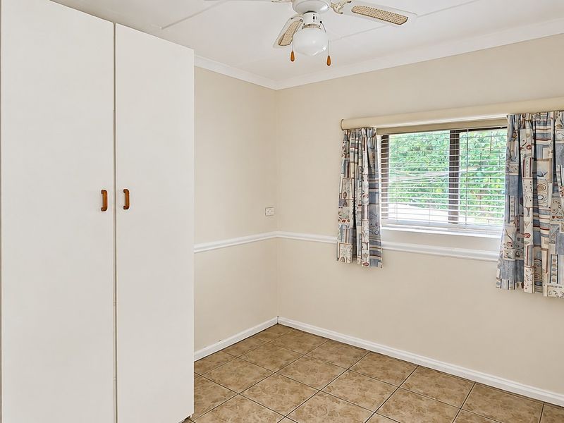 A bedroom featuring tiled flooring, a built-in wardrobe, and a ceiling fan, offering a neutral canvas for personalization.