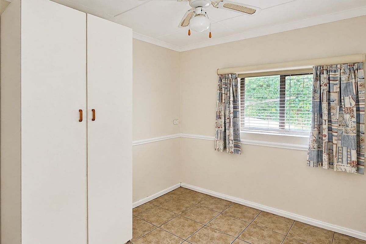 A bedroom featuring tiled flooring, a built-in wardrobe, and a ceiling fan, offering a neutral canvas for personalization.