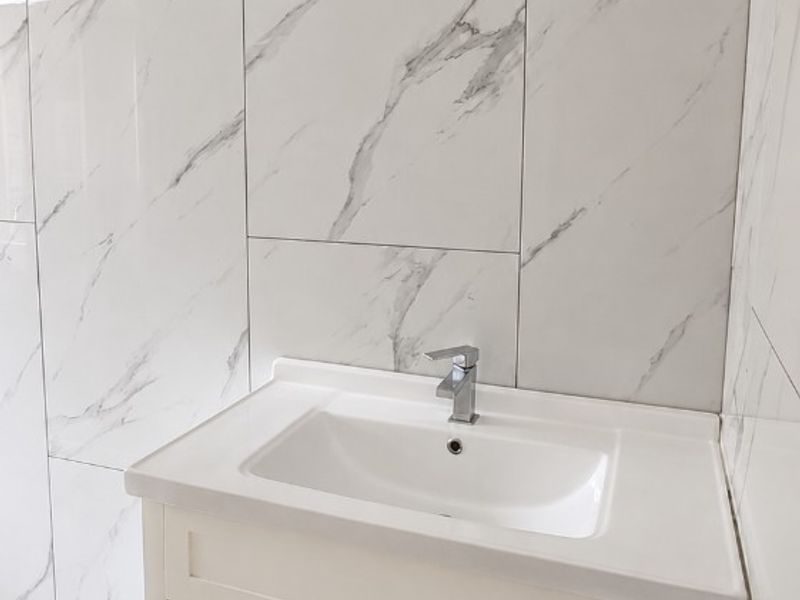 A modern bathroom vanity featuring a white cabinet, integrated ceramic basin, chrome mixer tap, and elegant marble-look wall tiling.