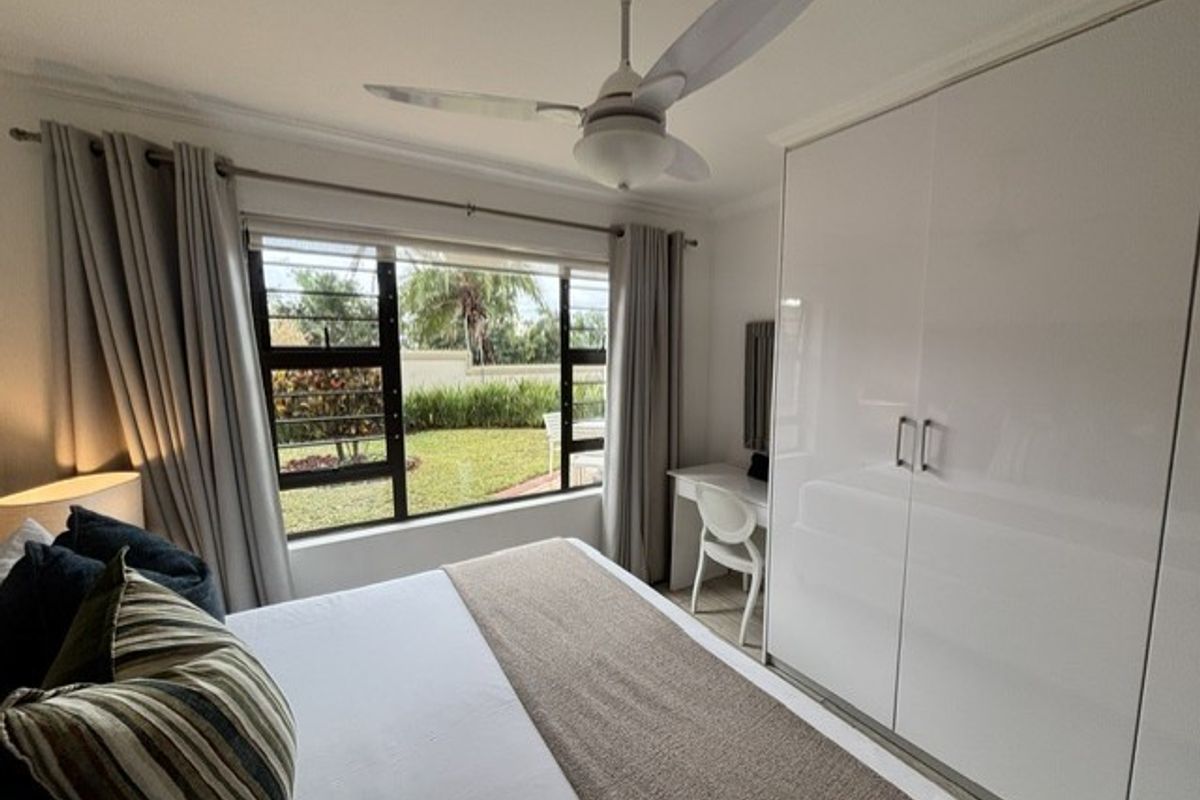 A well-maintained bedroom featuring a ceiling fan, large window with garden views, and sleek built-in wardrobes.