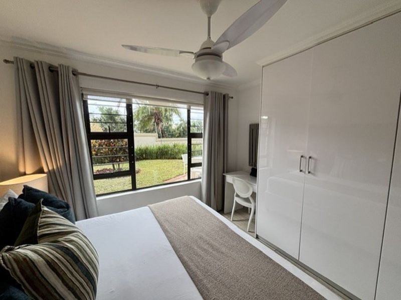 A well-maintained bedroom featuring a ceiling fan, large window with garden views, and sleek built-in wardrobes.