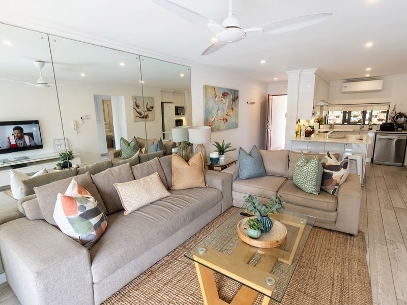 Bright open-plan living and kitchen area featuring tiled floors, a large mirrored feature wall, ceiling fans, and modern kitchen cabinetry.