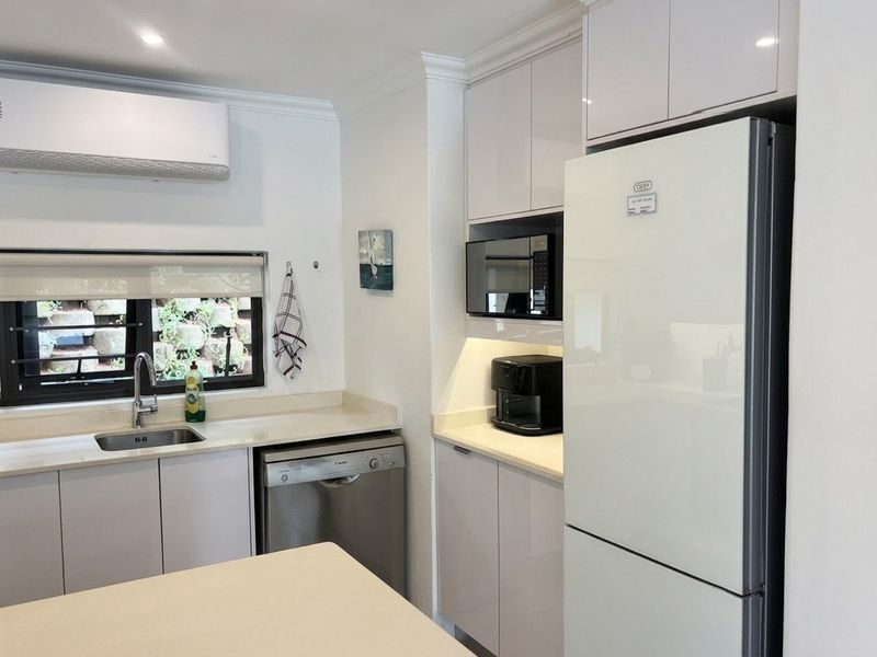 Modern kitchen featuring sleek high-gloss cabinetry, stone countertops, integrated microwave, and a wall-mounted air conditioning unit.
