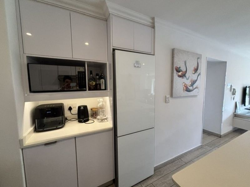 Modern kitchen area featuring sleek white cabinetry, integrated refrigerator, built-in microwave, and stone countertops with under-cabinet lighting.