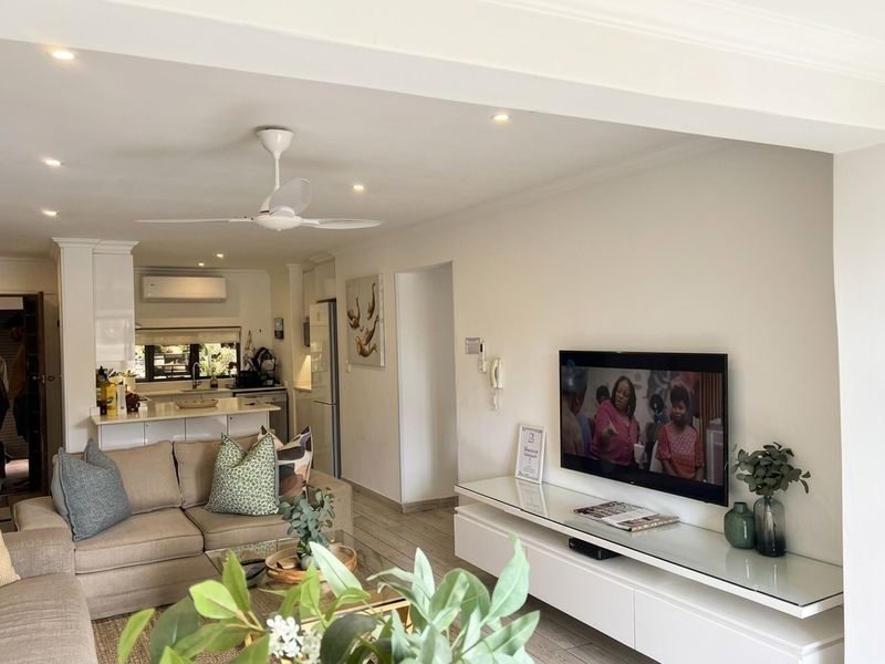 A bright open-plan living and kitchen area featuring modern cabinetry, recessed lighting, a ceiling fan, and air conditioning, creating a functional and cohesive living space.