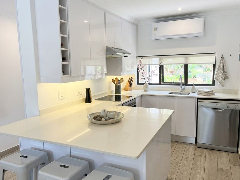 Modern kitchen featuring white gloss cabinetry, stone countertops, integrated appliances, and under-cabinet lighting, complemented by wood-look tile flooring and a split-system air conditioner.