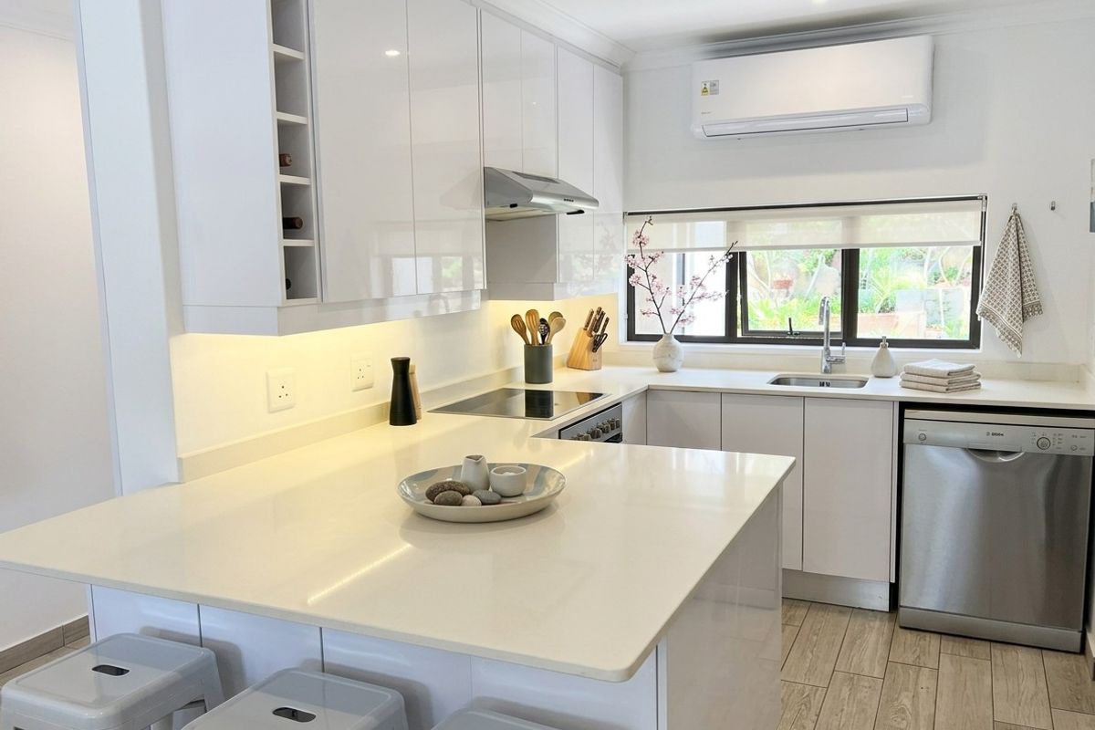 Modern kitchen featuring white gloss cabinetry, stone countertops, integrated appliances, and under-cabinet lighting, complemented by wood-look tile flooring and a split-system air conditioner.