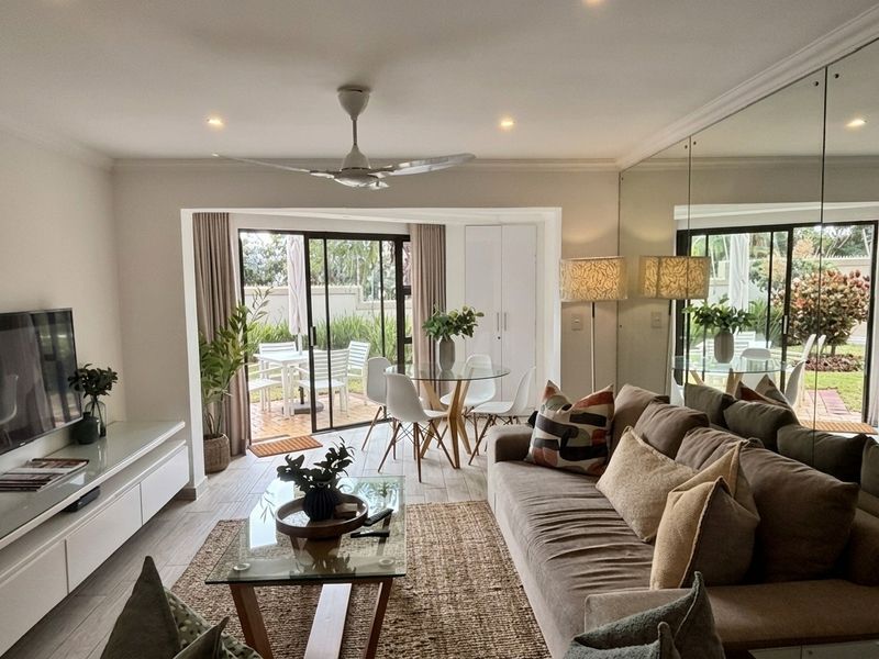 Bright open-plan living and dining area featuring tiled floors, a mirrored feature wall, ceiling fan, and direct access to a private patio.