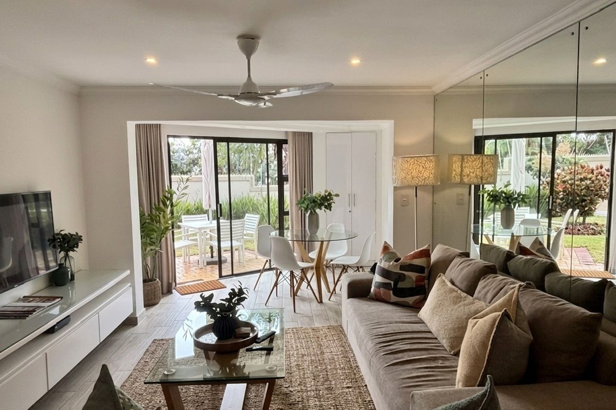 Bright open-plan living and dining area featuring tiled floors, a mirrored feature wall, ceiling fan, and direct access to a private patio.
