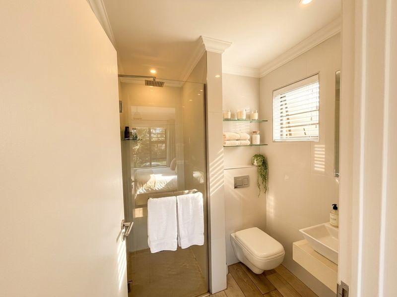 Modern bathroom featuring a glass-enclosed rain shower, wall-mounted toilet, vessel sink on a floating vanity, and neutral tiled finishes.