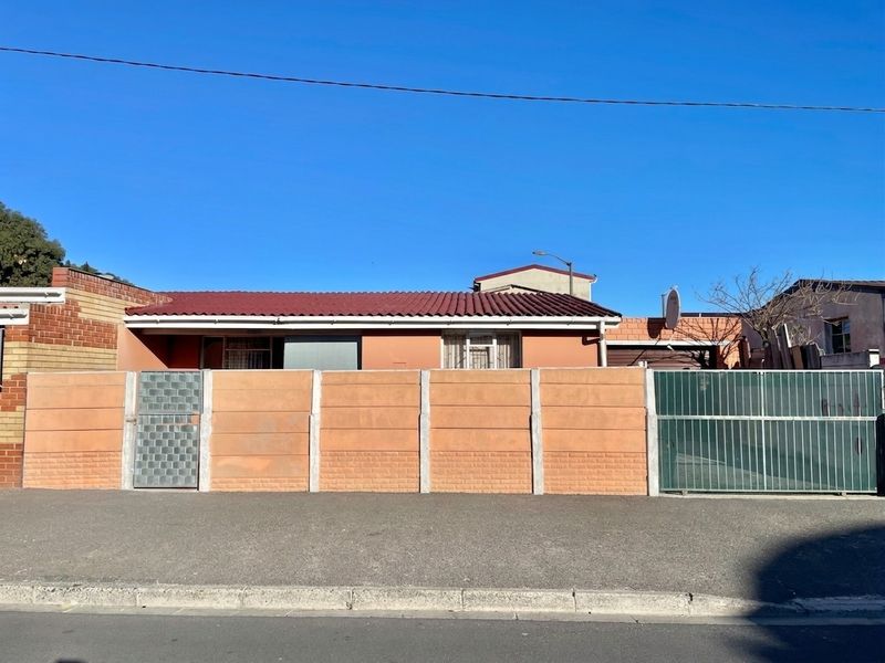 Front view of a single-story house featuring a precast concrete boundary wall, metal gates, and a tiled roof.
