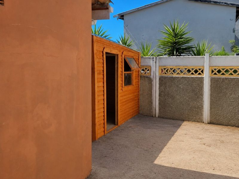 A rear exterior view featuring a wooden garden shed, a precast concrete boundary wall, and an open paved area.