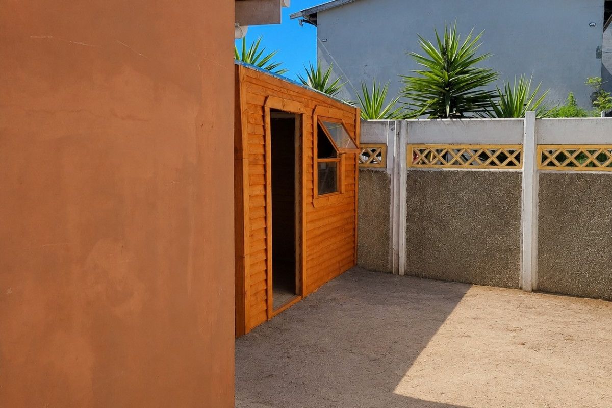 A rear exterior view featuring a wooden garden shed, a precast concrete boundary wall, and an open paved area.