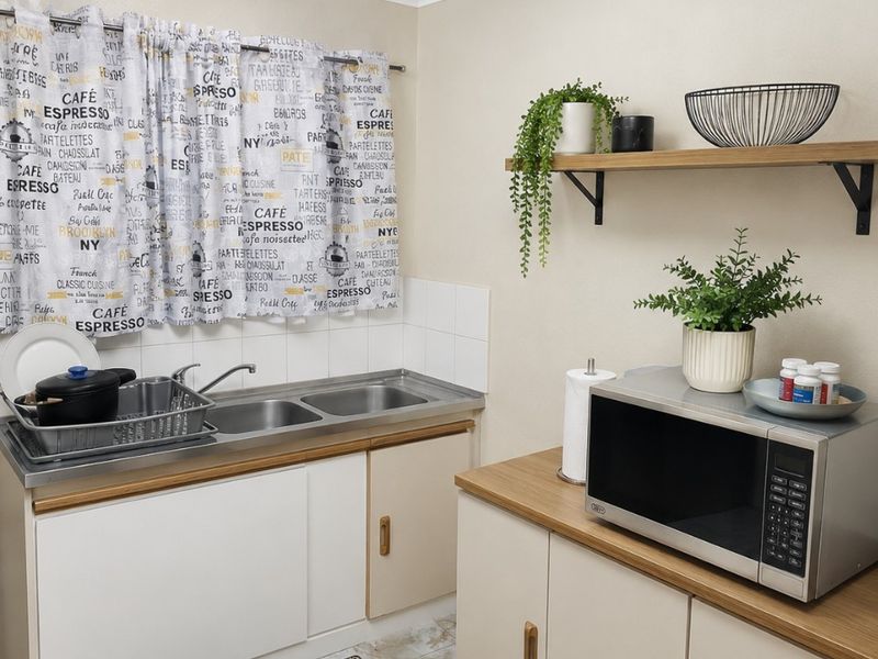 A functional kitchen area featuring double stainless steel sinks, laminate countertops, built-in cabinetry, and tiled flooring with a neutral wall finish.