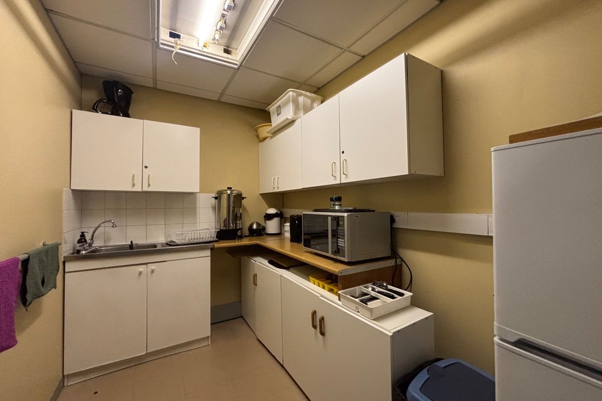 A functional office kitchenette featuring white cabinetry, a stainless steel sink, and a drop ceiling with integrated lighting.