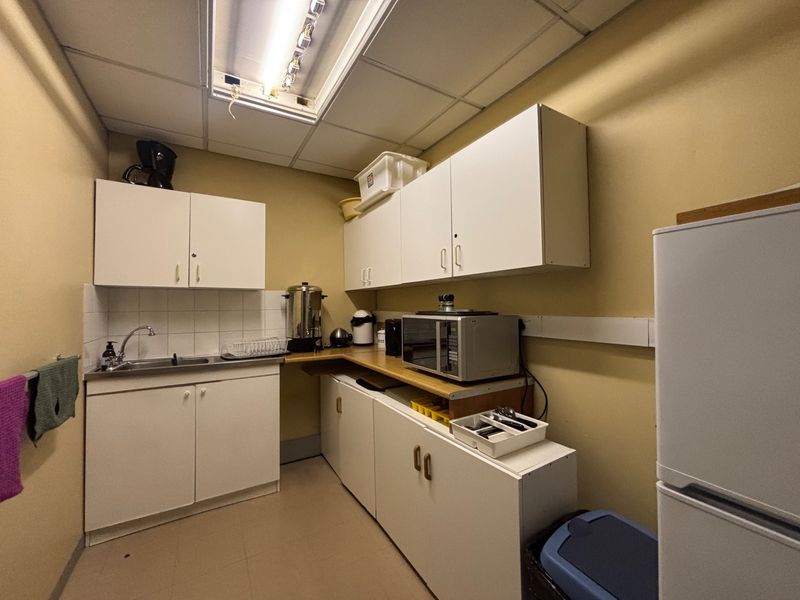 A functional office kitchenette featuring white cabinetry, a stainless steel sink, and a drop ceiling with integrated lighting.