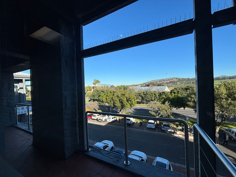 A covered balcony area featuring tiled flooring and a stainless steel balustrade, offering an elevated view of the street and surrounding landscape.