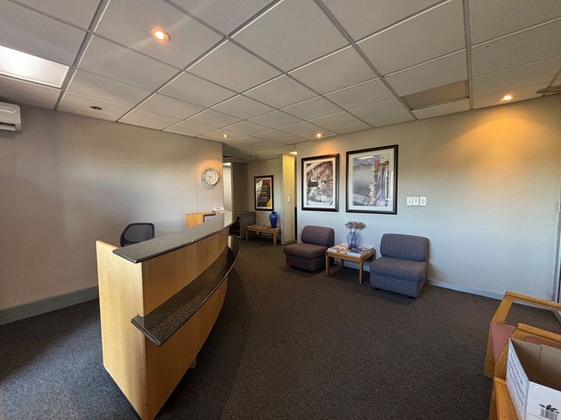 A professional office reception area featuring a built-in desk, suspended ceiling with recessed lighting, and carpeted flooring.
