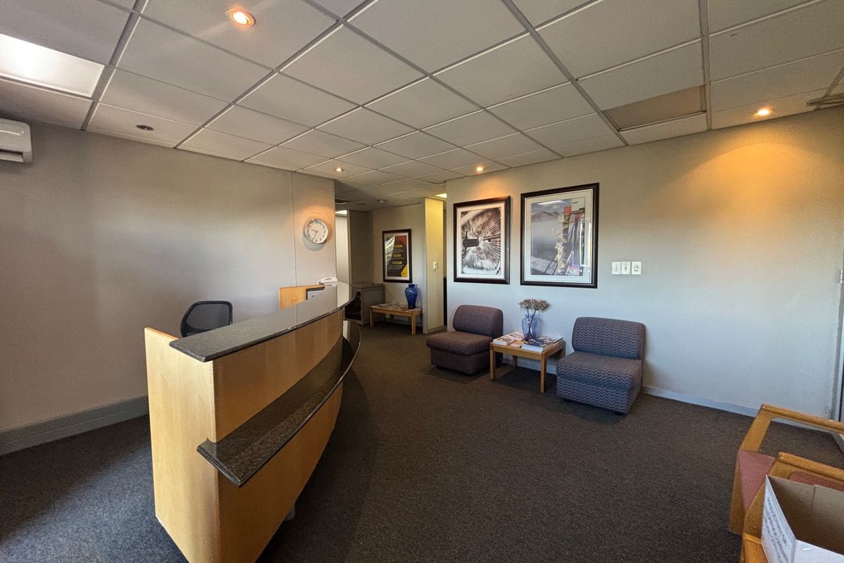 A professional office reception area featuring a built-in desk, suspended ceiling with recessed lighting, and carpeted flooring.