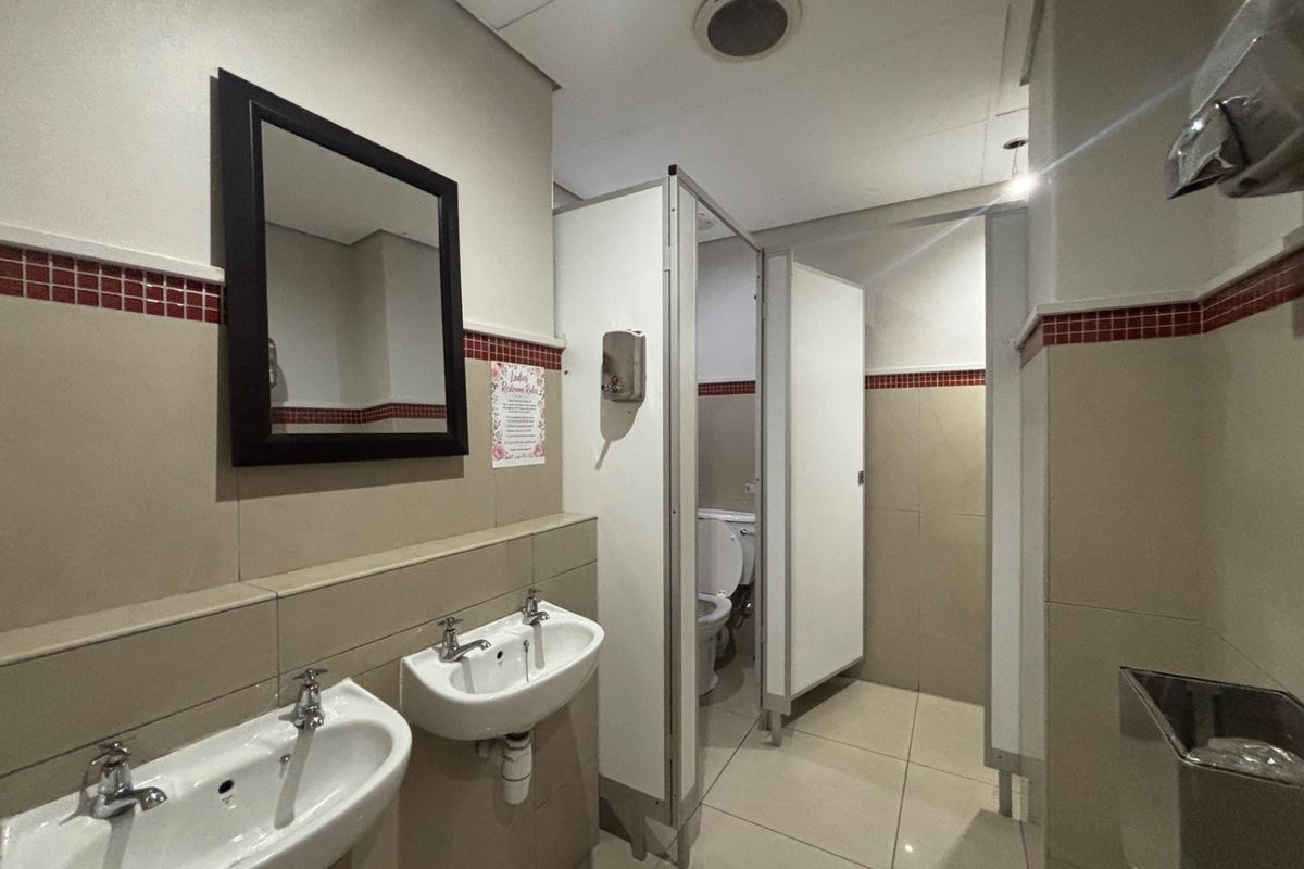 A functional office restroom featuring dual ceramic washbasins, tiled wall finishes with decorative accents, and private toilet cubicles.