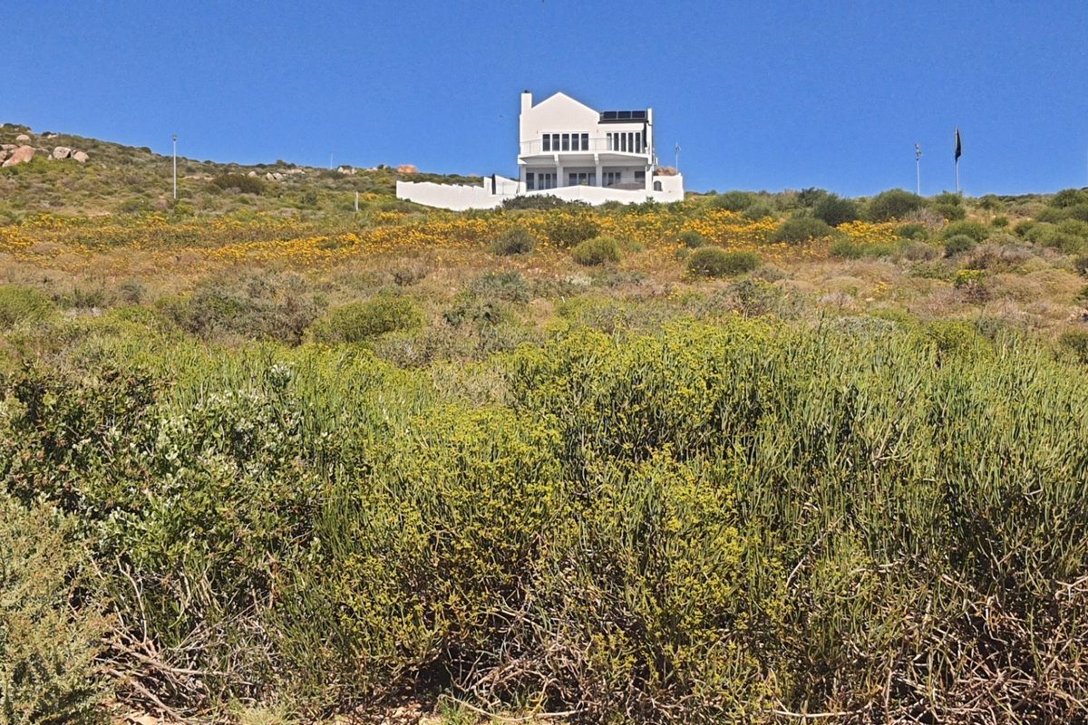 A view of a residential property situated on a sloped, natural landscape, featuring a white exterior, balcony, and roof-mounted solar panels.