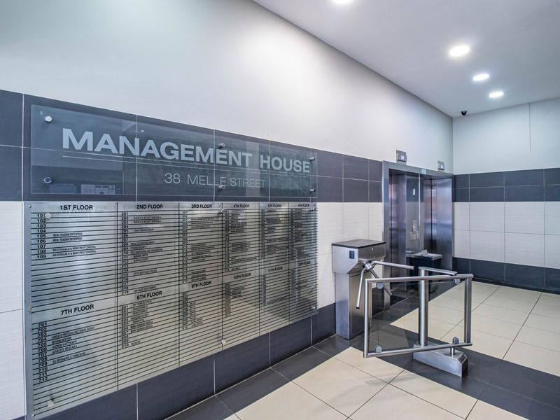 Modern commercial building lobby featuring a clear tenant directory board, secure turnstile access, and elevator bank with contemporary tiled finishes.