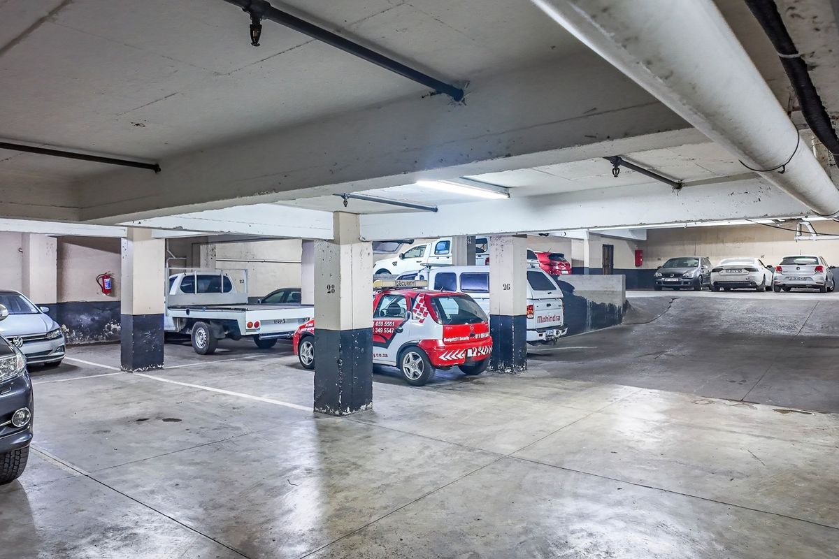 Underground commercial parking garage featuring concrete structural columns, overhead lighting, fire sprinkler system, and marked parking bays.