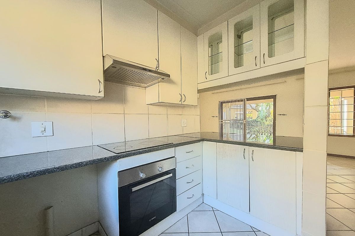 A functional kitchen featuring white built-in cabinetry, granite countertops, an integrated oven, and an electric hob, with tiled flooring throughout.